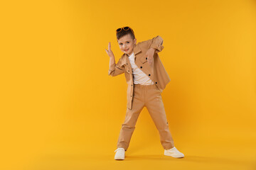 Happy little boy in sunglasses dancing on orange background. Space for text