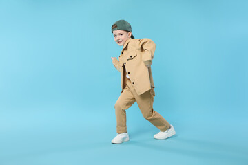 Happy little boy in baseball hat dancing on light blue background