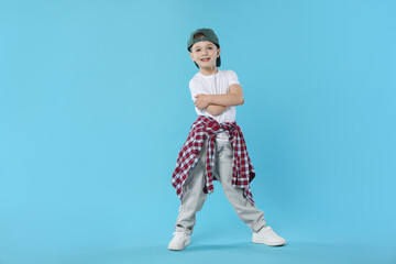 Happy little boy in baseball hat dancing on light blue background