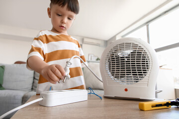 Little boy plugging electric heater into extension cord at home. Child in danger