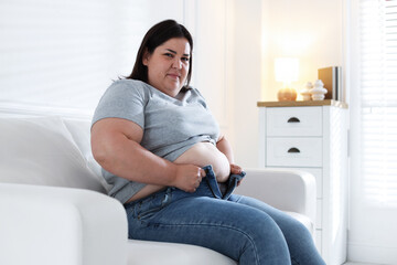 Overweight woman trying to put on tight jeans indoors