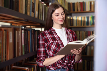 Woman reading book near shelves in public library