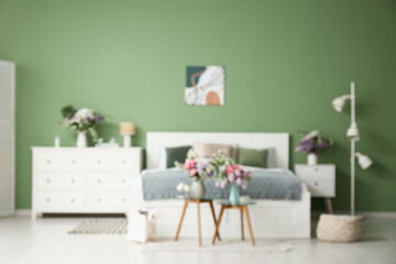 Blurred view of bedroom with comfortable bed and beautiful flowers