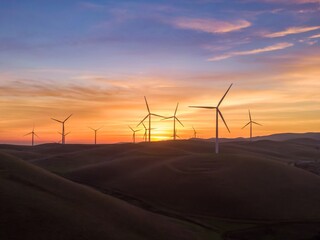 Wind turbines stand tall on rolling hills, harnessing wind energy at sunset in  Livermore,...