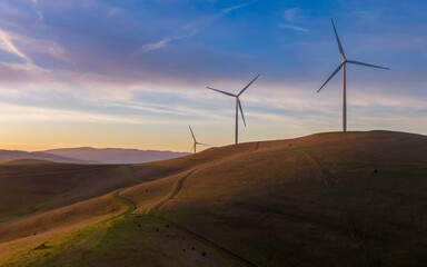 Wind turbines stand tall on rolling hills at sunset in Livermore, California, USA. These windmills...