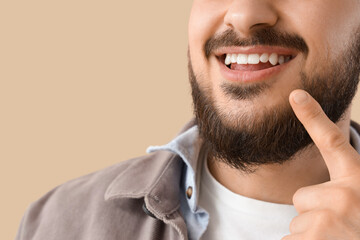 Young man pointing at his smile on beige background, closeup