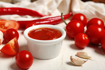Bowl of tasty ketchup with garlic and chili peppers on white wooden background, closeup