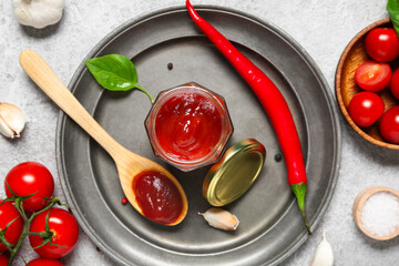 Jar and wooden spoon of tasty ketchup with different ingredients on grey background