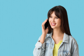Smiling young woman talking by mobile phone on blue background