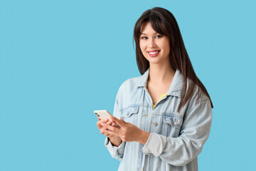 Smiling young woman using mobile phone on blue background