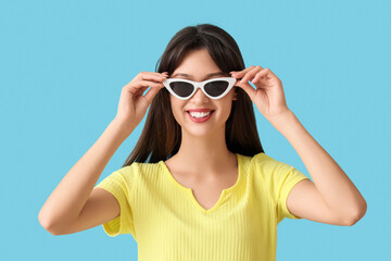 Smiling young woman in stylish sunglasses on blue background