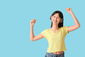 Smiling young woman in headphones dancing on blue background