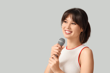 Happy young woman with microphone singing on light background