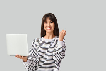 Smiling young woman with laptop on light background