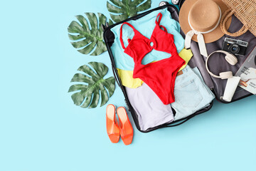 Open suitcase with beach accessories and palm leaves on blue background