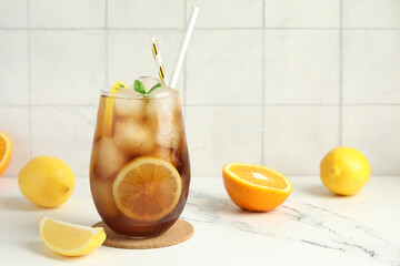 Glass of Long Island iced tea cocktail with mint and citrus fruits on white table
