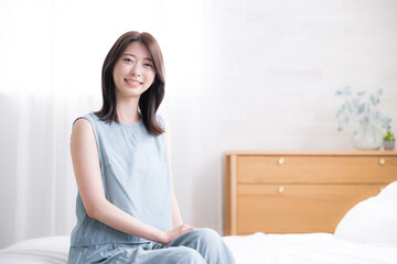 寝起きでベッドに座る女性の上半身　爽やかな朝のイメージ