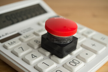 Closeup red emergency button on white calculator background. Financial crisis, bankrupt, loss, refinancing, debt restructuring, stop payment, risk management and so on concept.