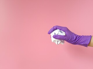 Hand in purple rubber protective glove holding crumpled paper on pink background