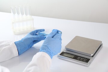 Scientist working with sample near scales at white table, closeup