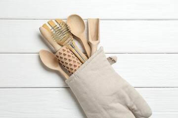 Different kitchen utensils in oven mitten on white wooden table, top view
