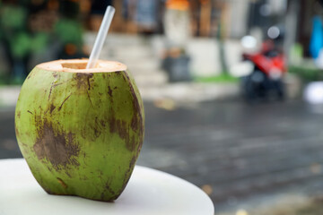 Green coconut with refreshing drink and straw on white table outdoors, closeup. Space for text