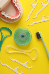 Different oral care products and dental model on yellow background, flat lay