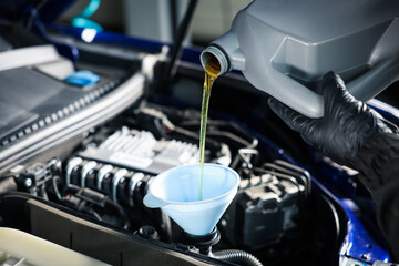 Worker pouring motor oil from canister into car engine, closeup