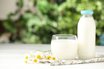 Fresh milk in glass, bottle and chamomile flowers on white wooden table outdoors, space for text. Dairy product