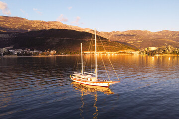 A sailboat glides peacefully across a calm lake, reflecting the warm hues of sunset. majestic mountains and a vibrant waterfront town provide a picturesque backdrop.