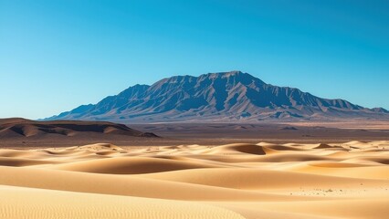 Sand dunes stretch toward mountains under a clear blue sky in the desert