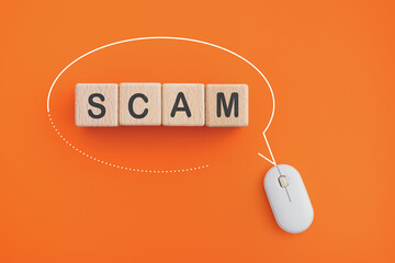 For investment scam, fraud and Ponzi scheme concept.  SCAM text   on wooden cube blocks inside speech bubble frame and wireless mouse on orange background