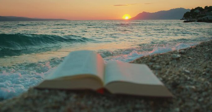 A book on a pebbled shore facing sea waves during sunset in summer Croatia