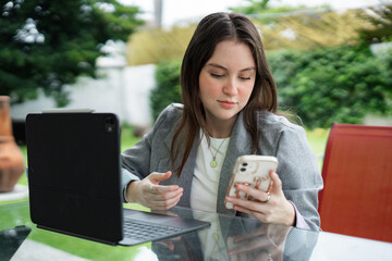 Young woman working remotely with tablet and smartphone outdoors