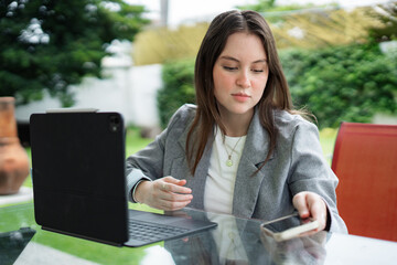 Young woman working remotely with tablet and smartphone outdoors