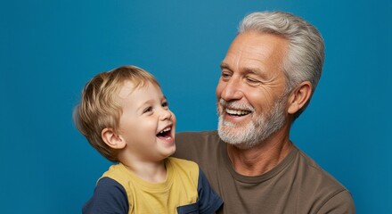A senior man and a young boy are together, both laughing heartily against a blue background.
