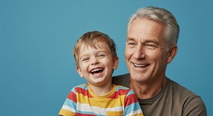 Grandfather and grandson smiling happily together in front of a blue background. Family love.