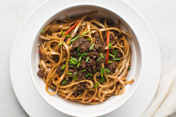 Overhead view of mongolian ground beef noodles in  a white bowl, top view of ground beef noodles with green and red pepper