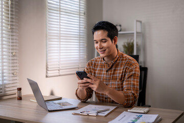 A man is sitting at a desk with a laptop and a cell phone