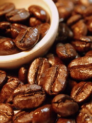 Close-up of roasted coffee beans with a white ceramic cup filled with beans, highlighting rich...