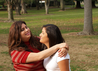Fototapeta premium Two Hispanic Sisters Embracing Outdoors In Park