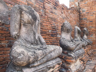 Ancient headless Buddha statues sitting in meditation posture against a weathered brick wall at a...