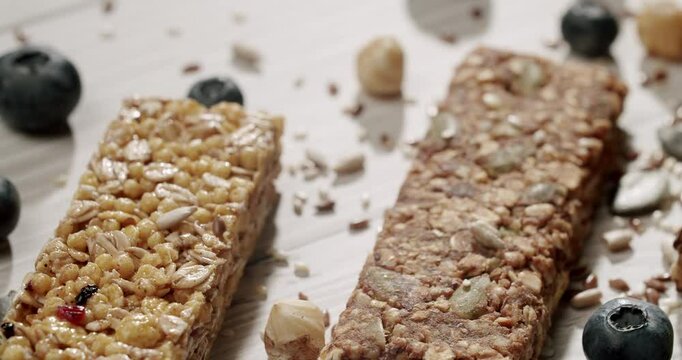 Close-up of two healthy granola bars with nuts and scattered blueberries on a wooden surface, showcasing nutritious ingredients. Assorted Granola Bars with Blueberries and Nuts on White Wooden Table