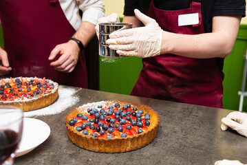 Chef dusting powdered sugar on berry tart.