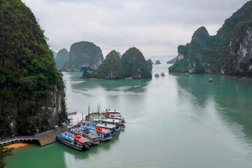 Traditional boats at Ha Long Bay pier, Vietnam, with limestone karsts and calm emerald waters under...