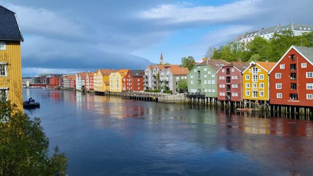 Peaceful spring scene of vibrant stilt houses along Trondheim&rsquo;s riverfront, their colorful fa&ccedil;ades mirrored in the softly rippling water on a calm day in Norway