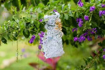 Lace bridal garter with blue ribbon detail hanging on a green branch with purple flowers. A...