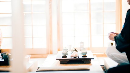Traditional Japanese tea ceremony setting with a person seated on tatami mats, surrounded by tea utensils and natural light, creating a serene and cultural atmosphere
