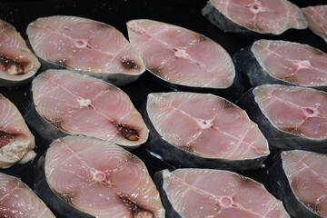 Slices of fresh raw fish arranged for sale at a seafood market, commonly used in cooking.