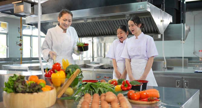 Culinary Students Practicing Cooking Skills with Instructor, Young Chefs Learning and Cooking in a Professional Kitchen, Young Female Cooks Preparing Food in a Commercial Kitchen
